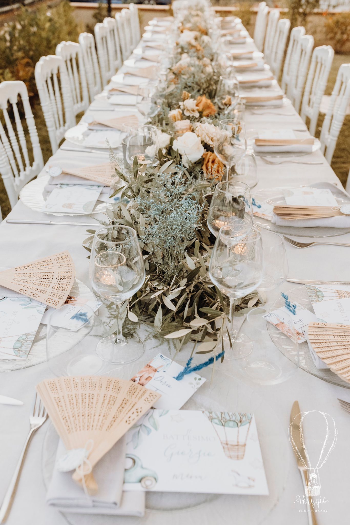 Centrotavola basso su tavolo imperiale con foglie di ulivo, fiori azzurri essiccati e rose caramello