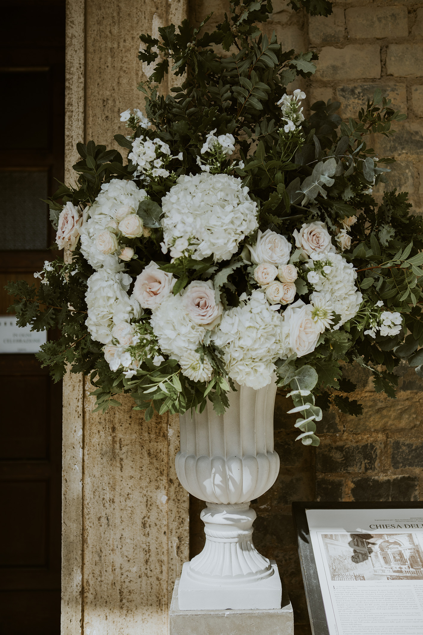 Grande urna bianca all'ingresso della chiesa, con ortensie e rose bianche e verdi misti