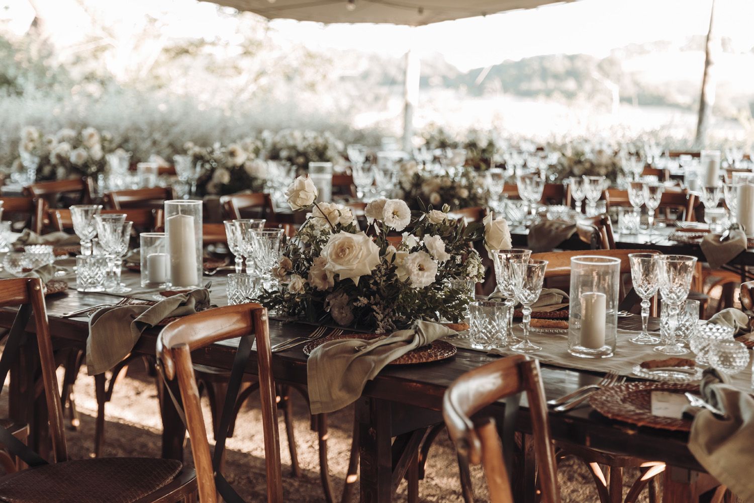 Allestimento tavoli da matrimonio in legno con centrotavola composto da fiori bianchi e verde