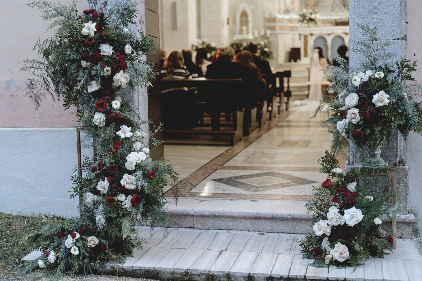 Decorazione floreale ingresso chiesa per matrimonio in inverno, con verdi di stagione e rose bianche e rosse