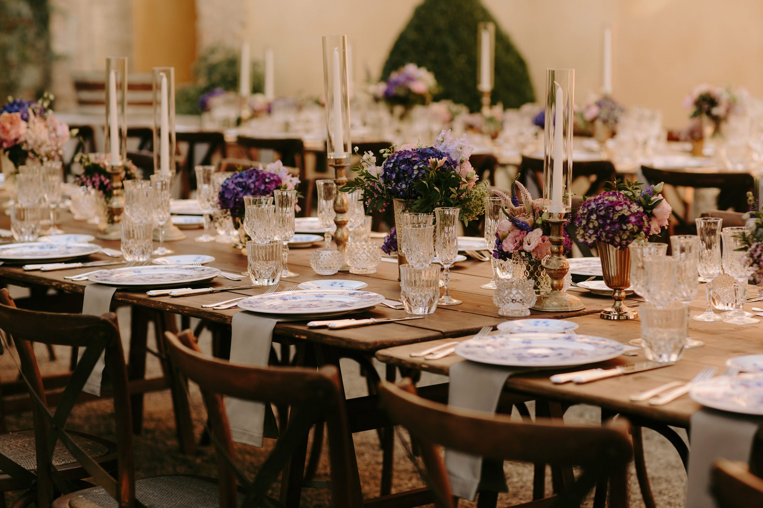 Ricevimento di matrimonio all'aperto in stile italiano, con tavoli in legno, porcellane, candele e fiori di campo