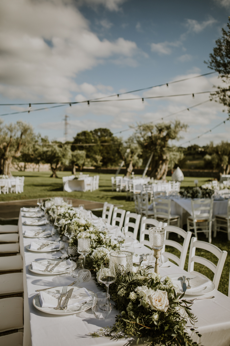 Centrotavola basso e lungo con fiori bianchi e verdi per matrimonio all'aperto in Puglia