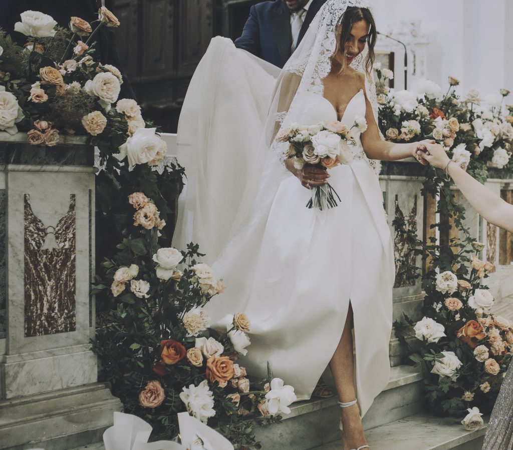 La sposa con il suo bouquet in chiesa circondata da fiori color terracotta, rosa cipria e bianco